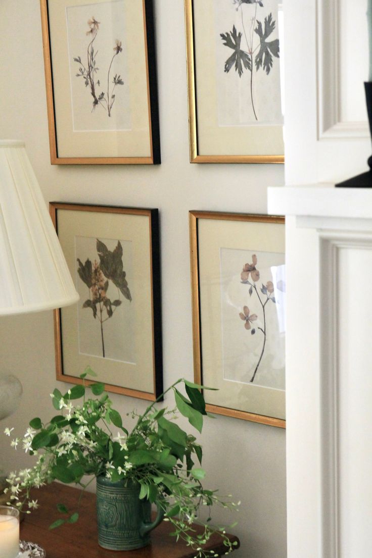 a table with flowers and plants on it in front of some framed pictures above the fireplace