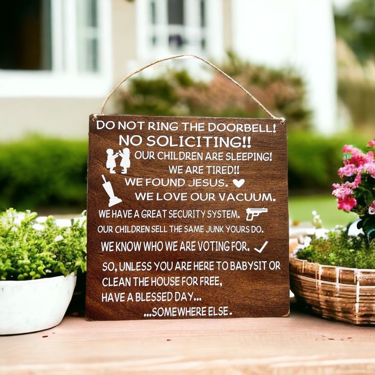 a wooden sign sitting on top of a table next to potted plants and flowers