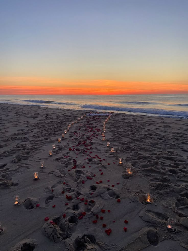 candles are lined up in the sand on the beach as the sun sets over the ocean