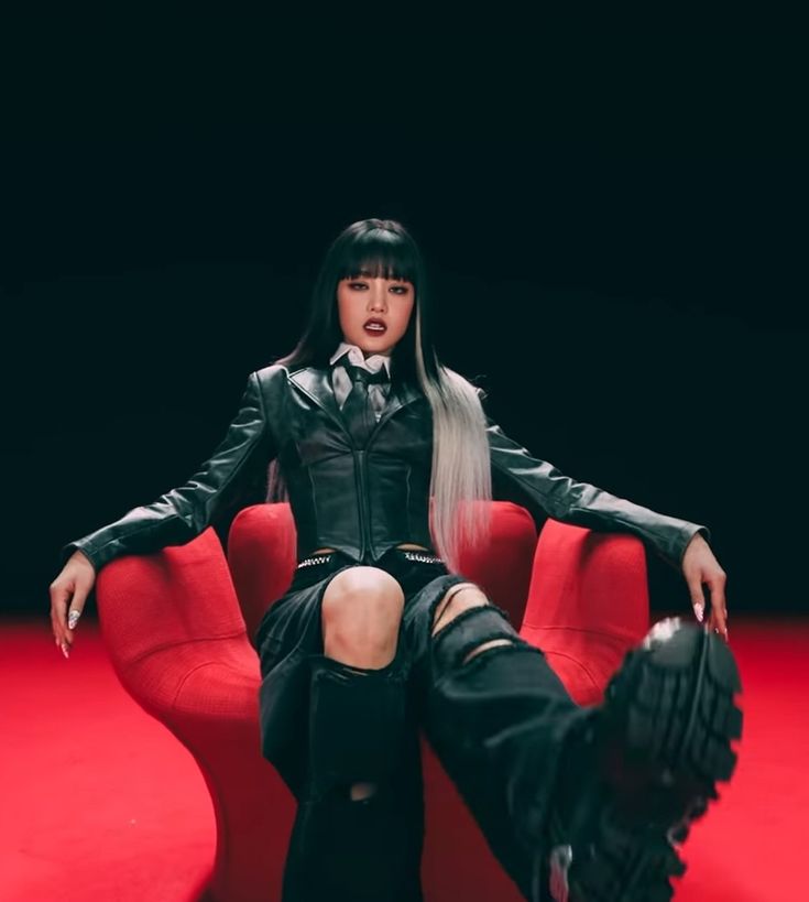 a woman sitting on top of a red chair with her legs crossed and wearing black boots