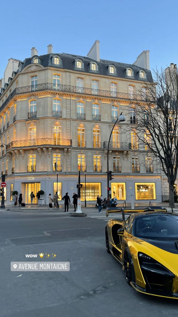 a yellow and black sports car parked in front of a tall building with lots of windows