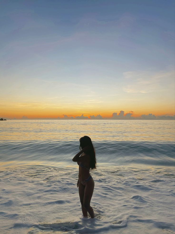 a woman standing in the ocean at sunset