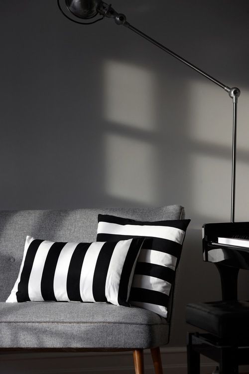 black and white striped pillows sit on a gray couch in front of a wall lamp