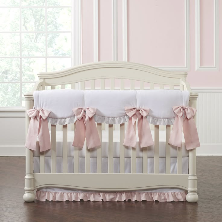 a white crib with pink bows on the top and bottom, in front of a window