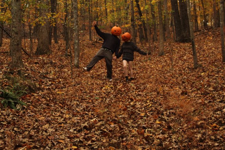 two people are running through the leaves in the woods with orange hats on their heads