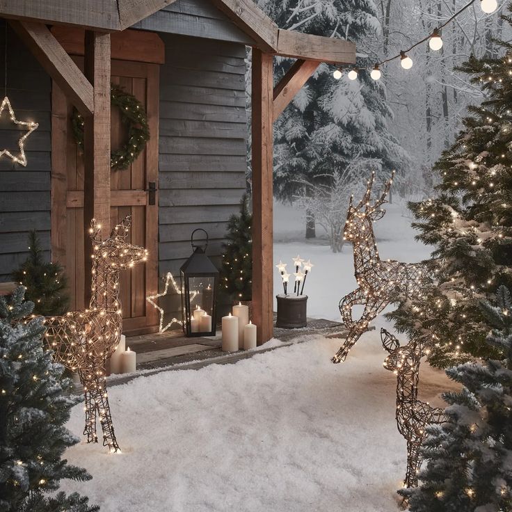 an outdoor christmas scene with lights and deer statues in the snow, surrounded by evergreen trees