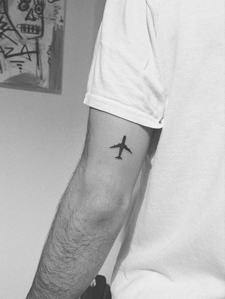 a man with a small airplane tattoo on his left arm and right hand, in black and white