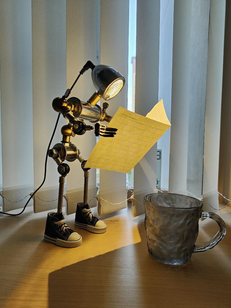 a lamp that is on top of a table next to a cup and some kind of paper