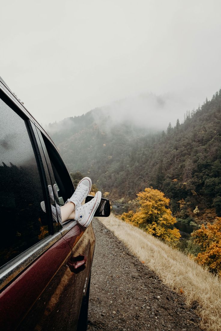 a person's feet sticking out the window of a car on a mountain road