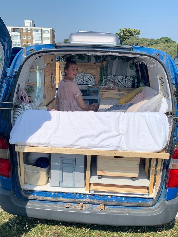 a woman sitting in the back of a blue van with mattresses on it's bed