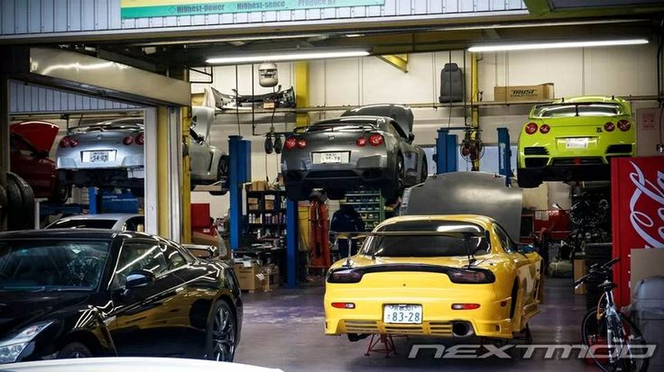 two cars parked in a garage next to each other with their hoods open and the lights on