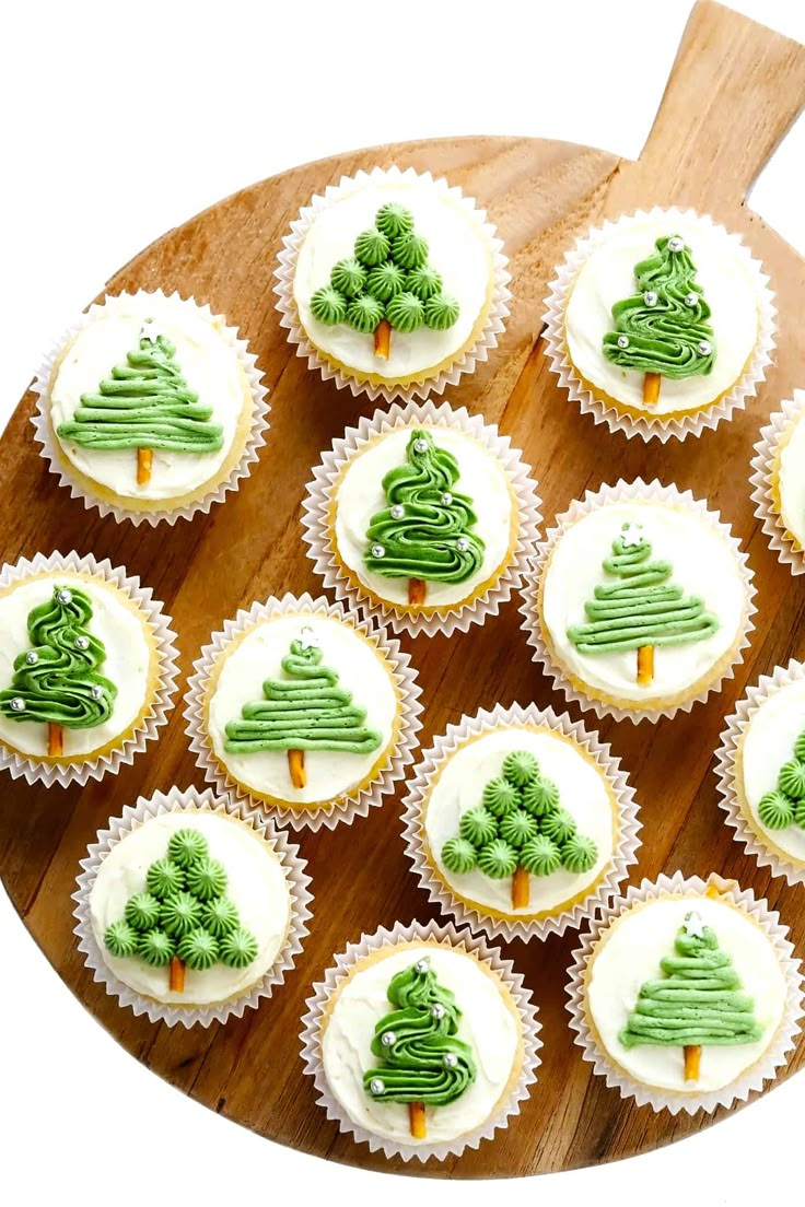 cupcakes decorated with green icing and trees on a wooden platter next to a cutting board