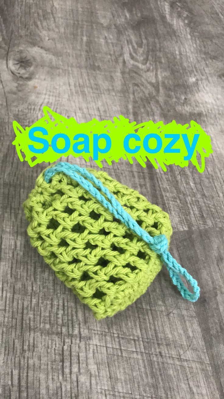 a green crochet pouch sitting on top of a wooden table with the words soap cozy written above it