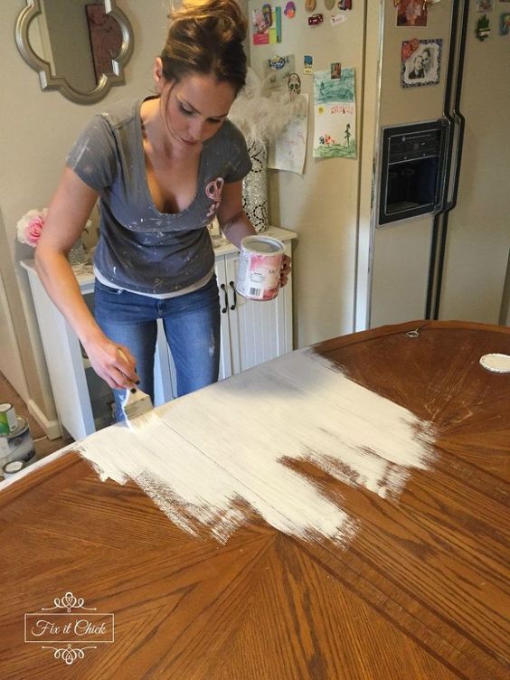 a woman is painting the top of a wooden table in her kitchen with white paint