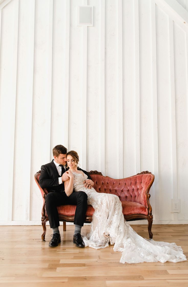 a bride and groom are sitting on a red couch in front of a white wall