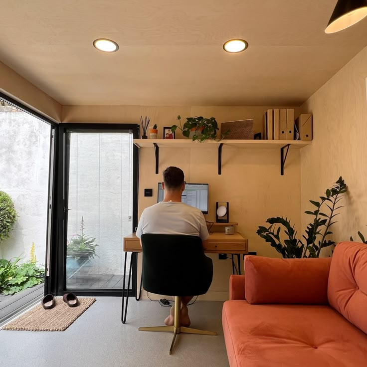 a person sitting at a desk in front of a window with plants on the shelves