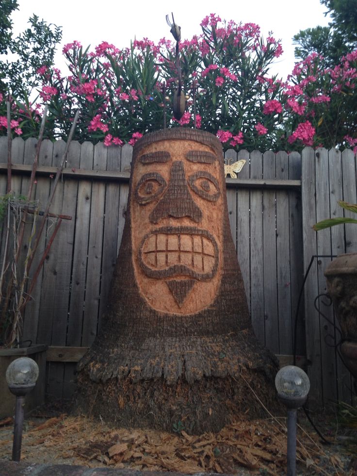 a wooden carving of a man's face on top of a tree stump in front of a fence