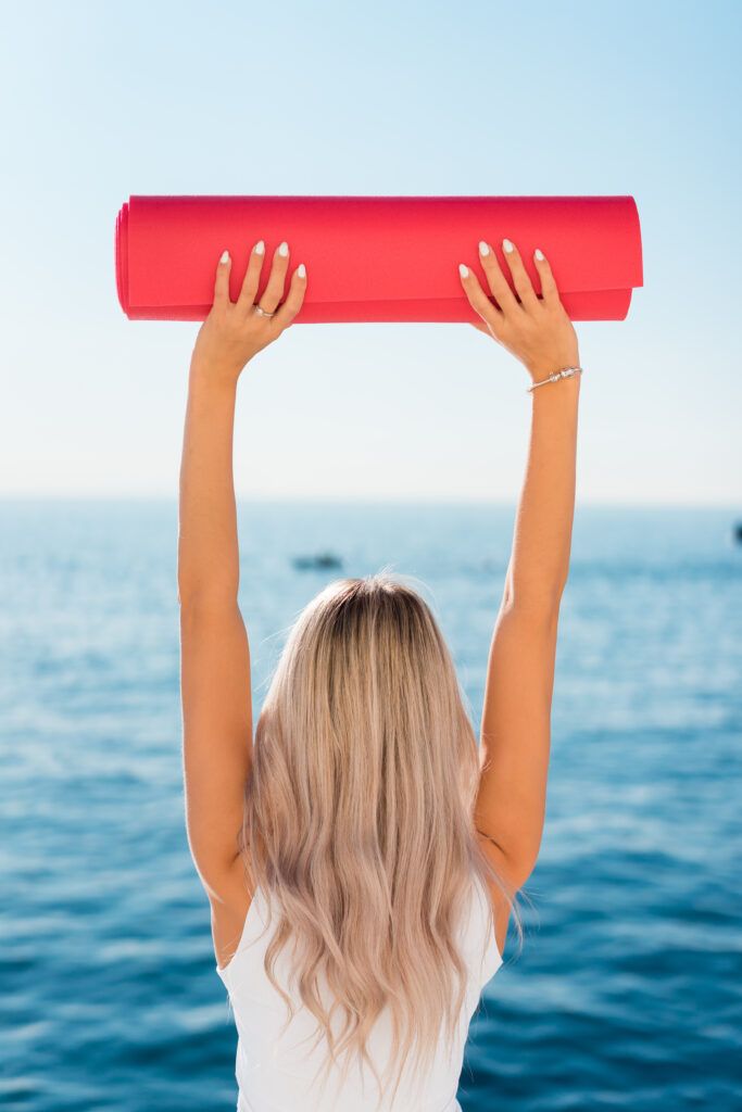 a woman holding up a large red object over her head in front of the ocean