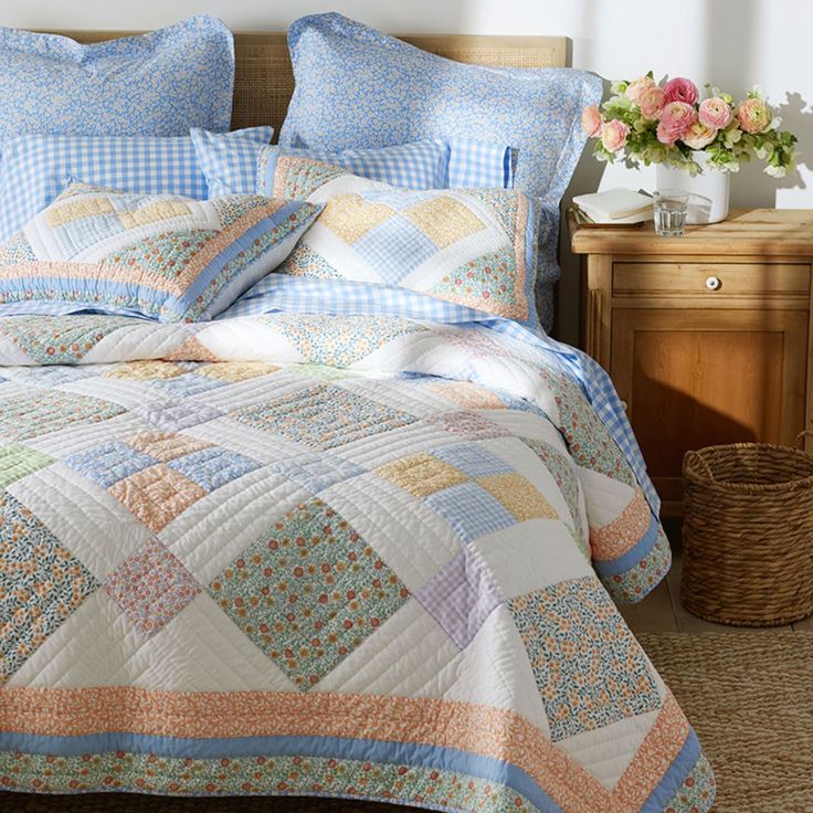 a bed covered in blue and white quilts next to a nightstand with flowers on it