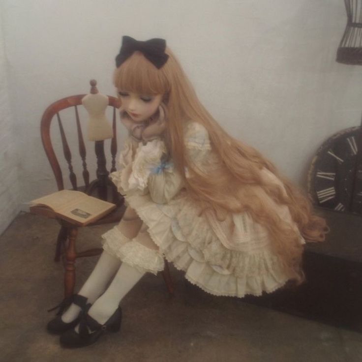 a doll sitting on a chair next to a table with an open book and clock