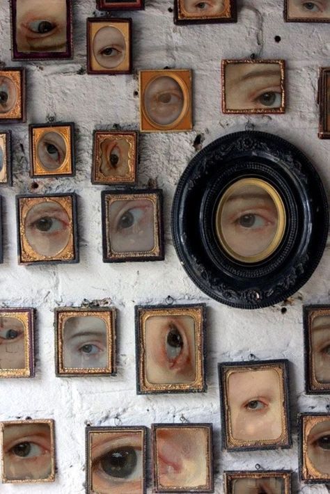 a wall with many framed pictures and an eyeball on it