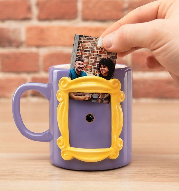 a hand holding a purple and yellow coffee mug with two photos in the middle, on top of a wooden table