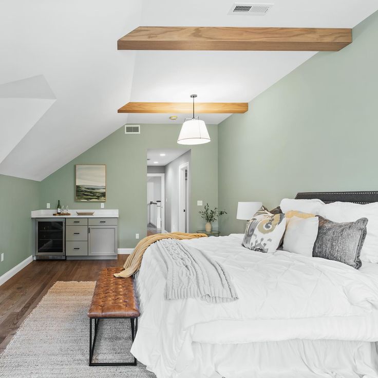 a bedroom with green walls, white bedding and wooden beams in an attic style home