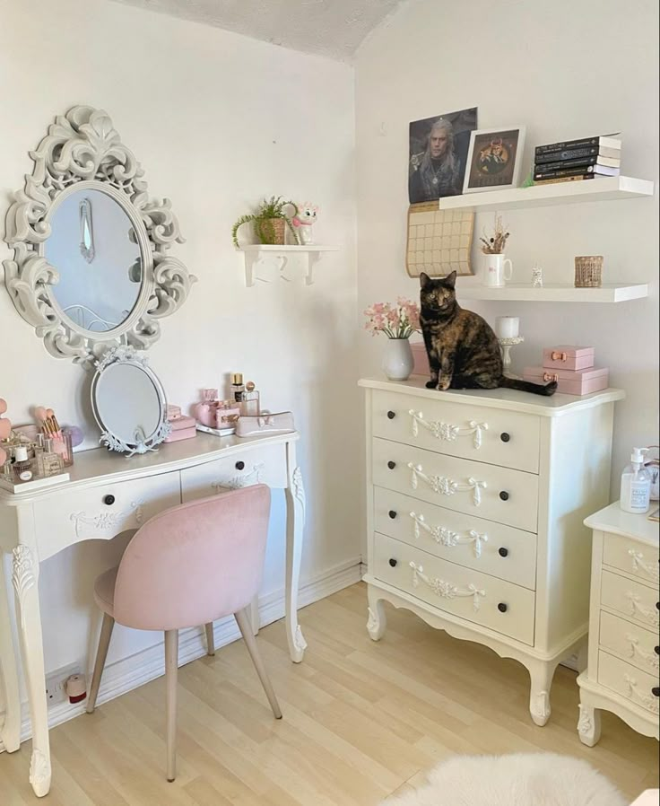 a cat sitting on top of a white dresser next to a pink chair and mirror