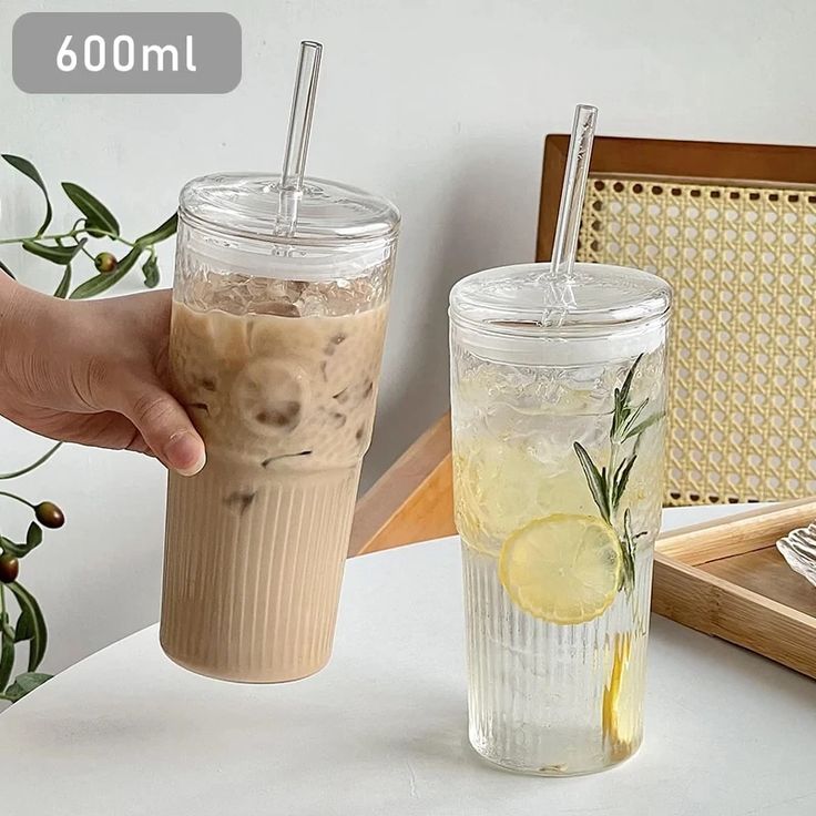 a hand holding a cup with a drink in it next to another cup on a table