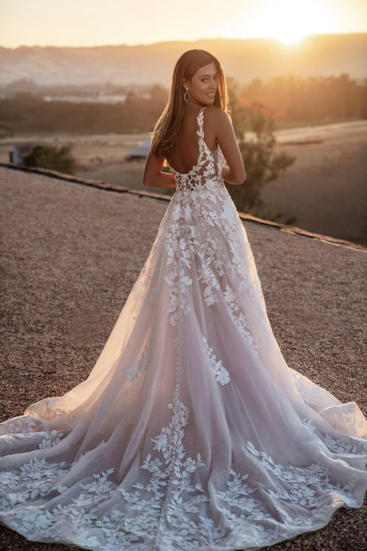 a woman standing on top of a dirt field wearing a wedding dress with white flowers