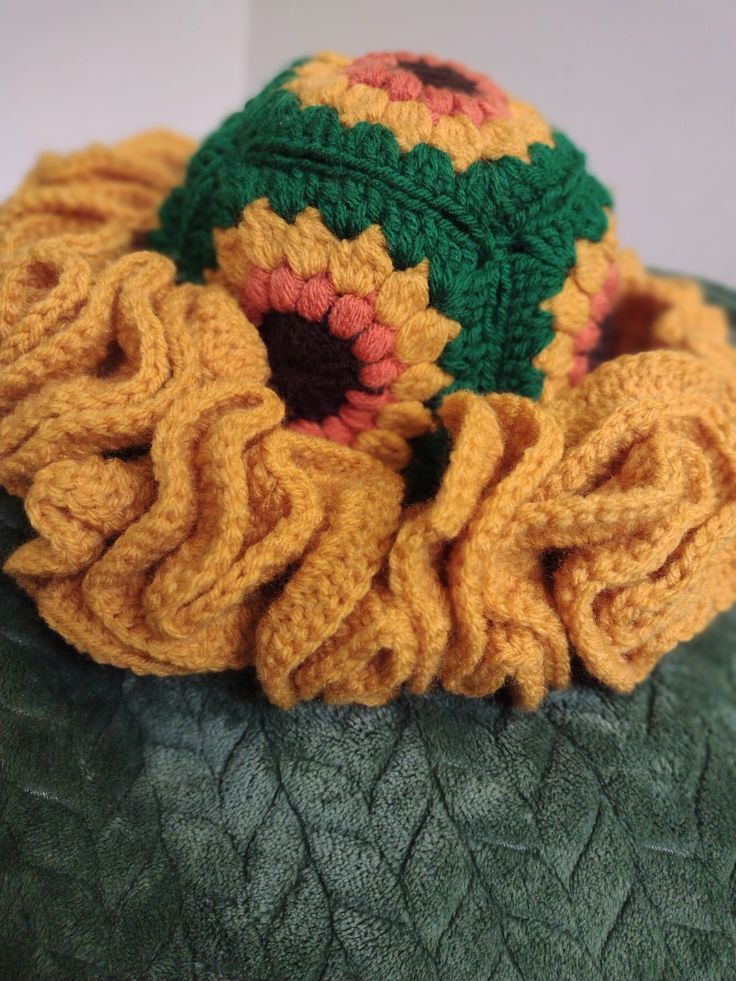 a crocheted sunflower sits on top of a green cushion with a yellow flower in the center