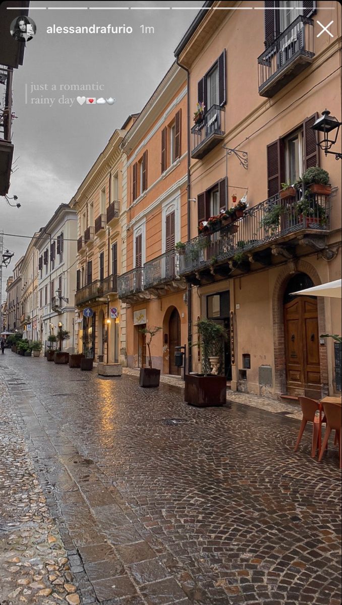 an empty cobblestone street with tables and umbrellas on it in the rain