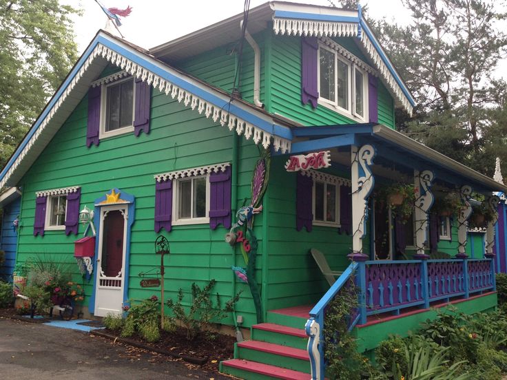 a green house with purple and blue shutters on the front, and stairs leading up to the second floor