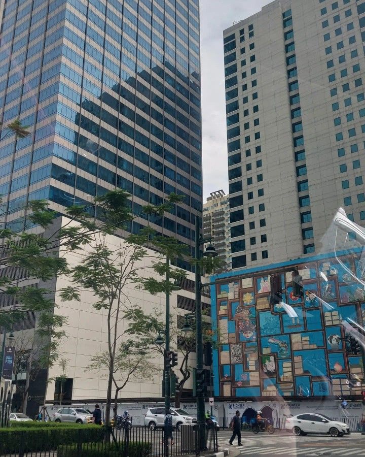 two tall buildings next to each other in front of trees and people walking on the sidewalk