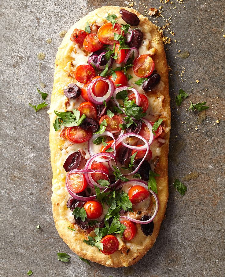 a pizza topped with tomatoes, onions and herbs on top of a stone countertop