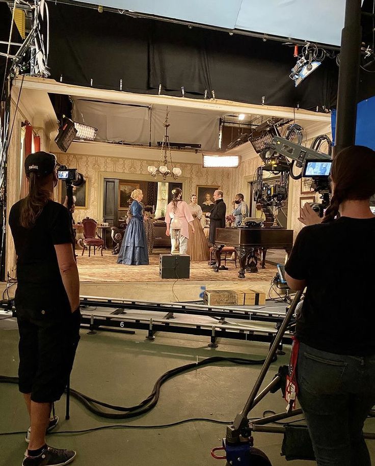 two women are standing in front of a camera set up for a movie with other people behind them