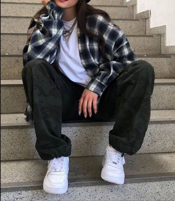 a person sitting on some steps with their feet crossed and wearing white sneakers, black pants and a plaid shirt