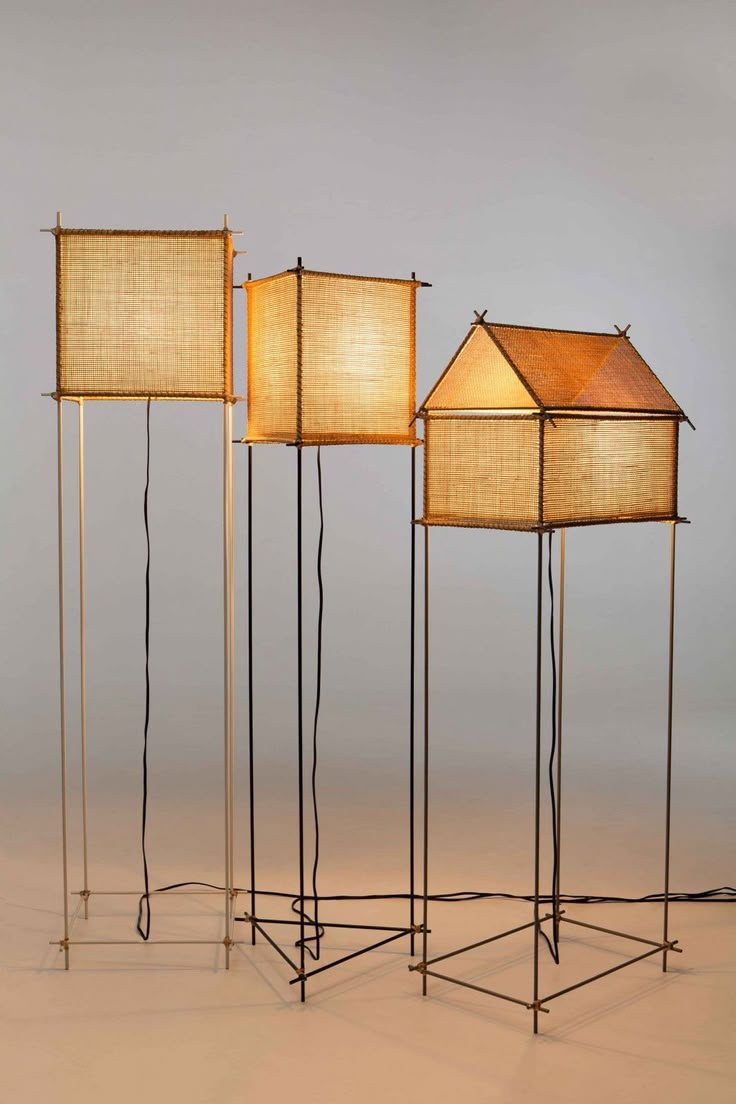 three floor lamps with shades on them in the shape of houses, and one light is turned on