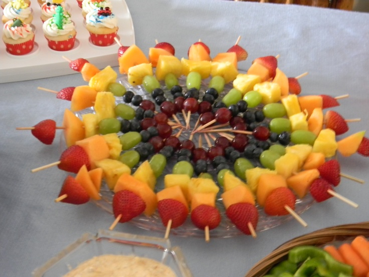 an assortment of fruits arranged on skewers with cupcakes in the background