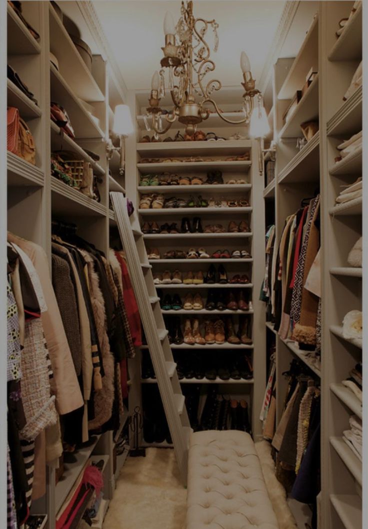 a walk in closet with lots of clothes and shoes on the shelves, chandelier hanging from the ceiling