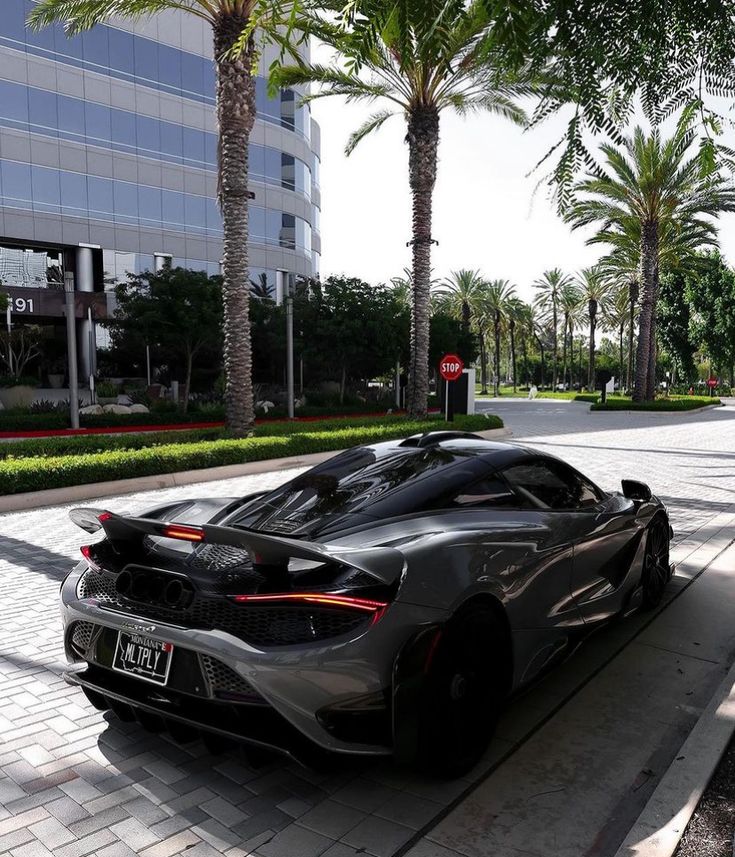 a grey sports car parked on the side of a road next to palm trees and buildings