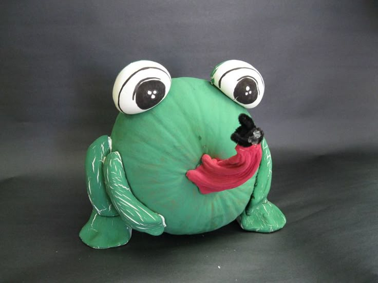 a green stuffed frog with big eyes sitting on a black surface and looking at the camera