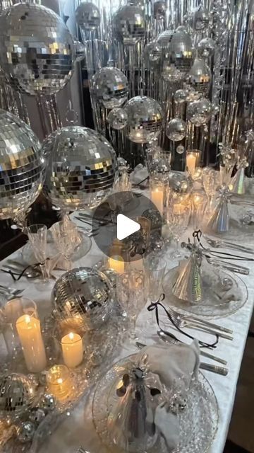 a table topped with lots of silver plates covered in disco ball decorations and candles on top of it