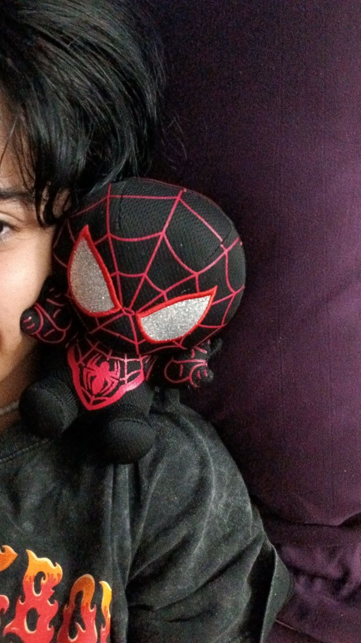 a young boy laying on top of a bed next to a spider man stuffed animal