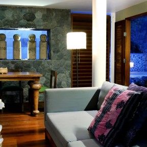 a living room filled with furniture next to a wooden table and wall covered in stone