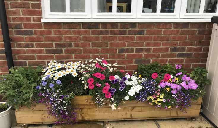 a wooden planter filled with lots of flowers next to a brick wall and door