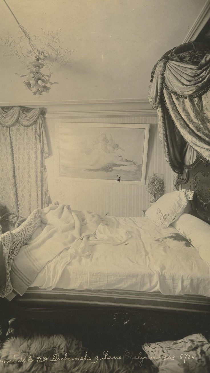 an old black and white photo of a bed in a room with drapes on the windows