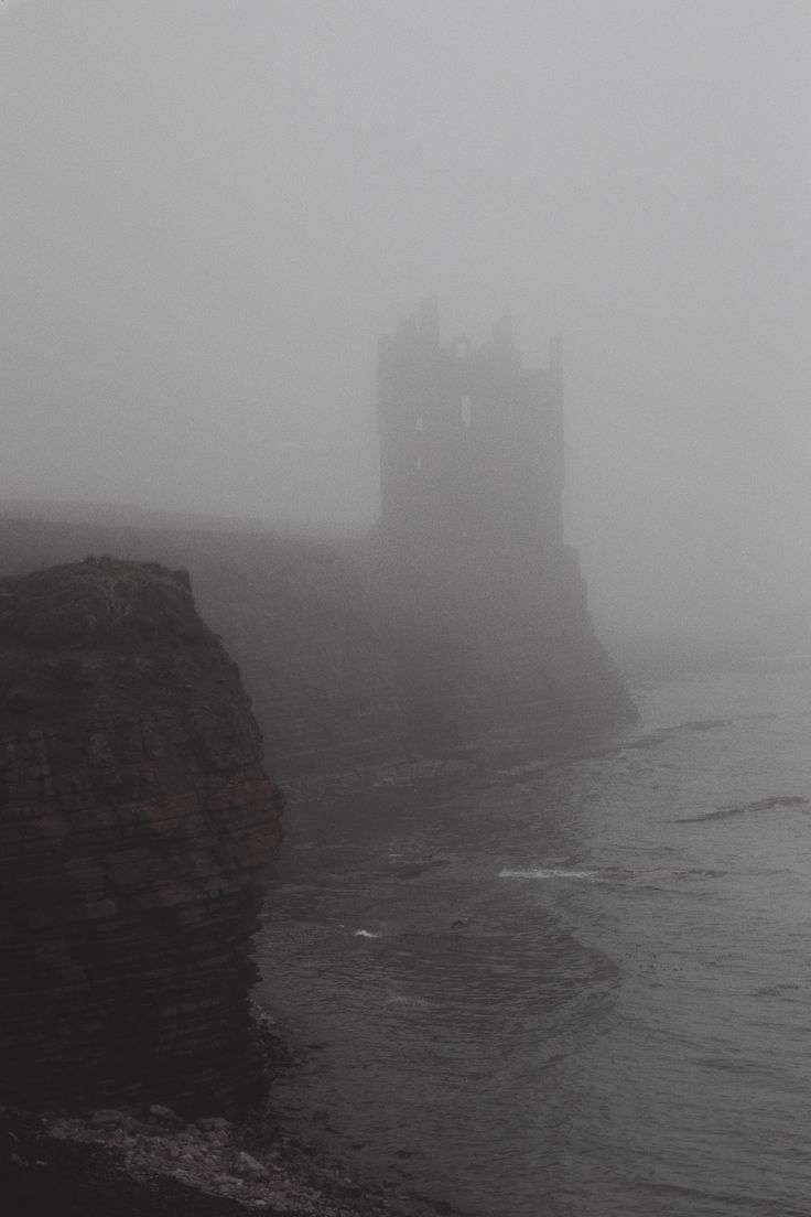 a castle sitting on top of a cliff next to the ocean in foggy weather