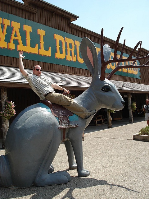 a man riding on the back of an antelope statue in front of a store