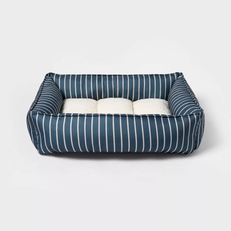 a blue and white striped dog bed with two pillows on the bottom, in front of a